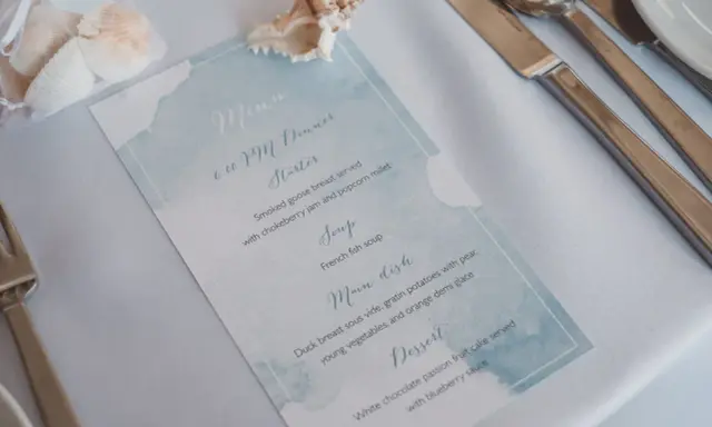 Menu weselne z akwarelowym motywem morskim, ozdobione muszlami.