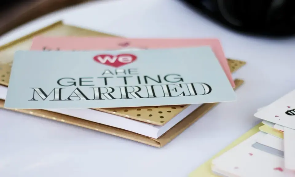 Zaproszenia ślubne "We are getting married" w formacie B0, ułożone na złotym notesie.