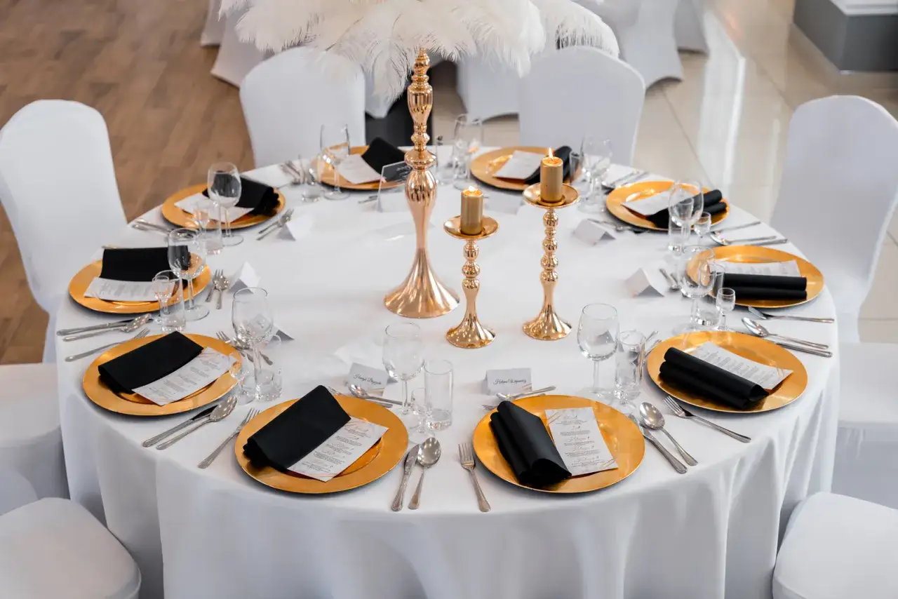 Eleganckie nakrycia stołu z złotymi talerzami i czarnymi serwetkami, świecami i piórami tworzą wykwintne motywy ślubne.