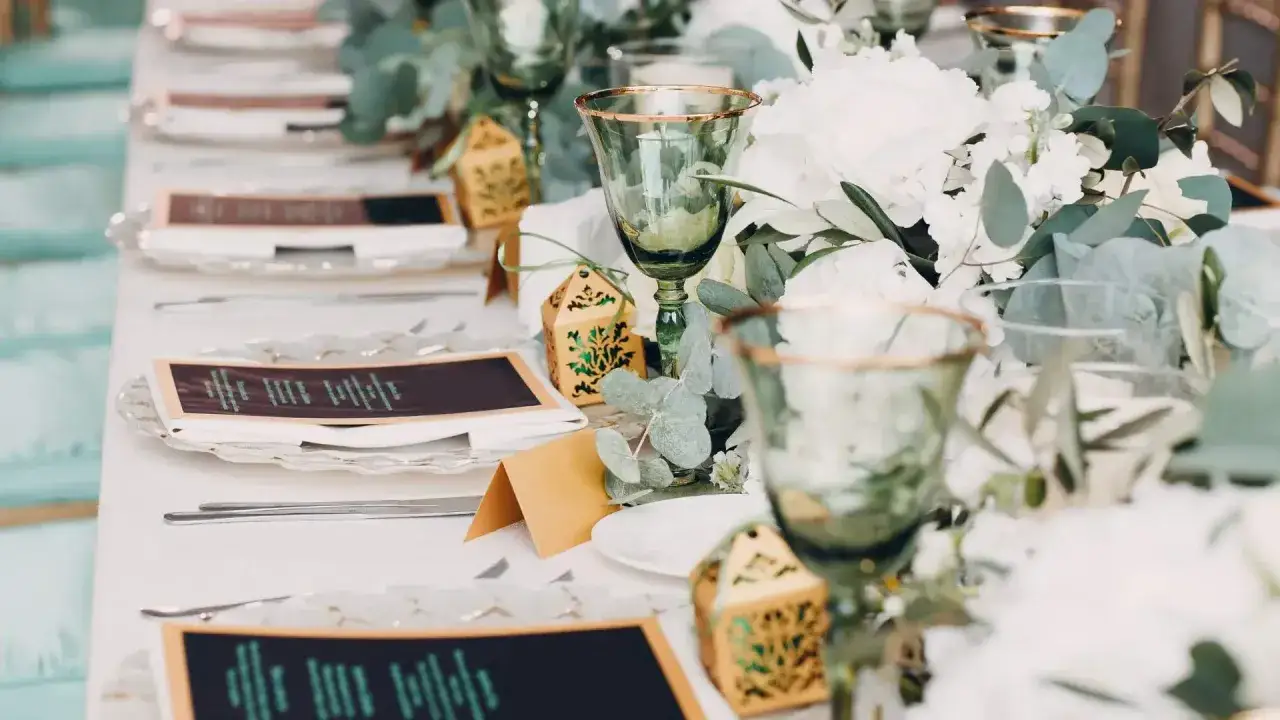 Eleganckie nakrycia stołu na wesele bez alkoholu: zielone kieliszki, menu, ozdobne pudełeczka i bukiety z eukaliptusem.