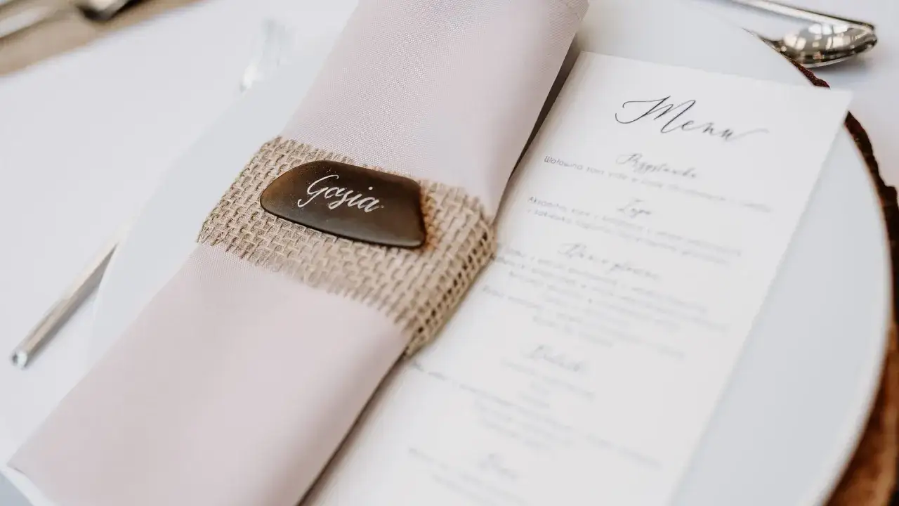 Eleganckie ręczne wypisywanie zaproszeń ślubnych. Na talerzu leży różowa serwetka z lnianym pierścieniem i tabliczką