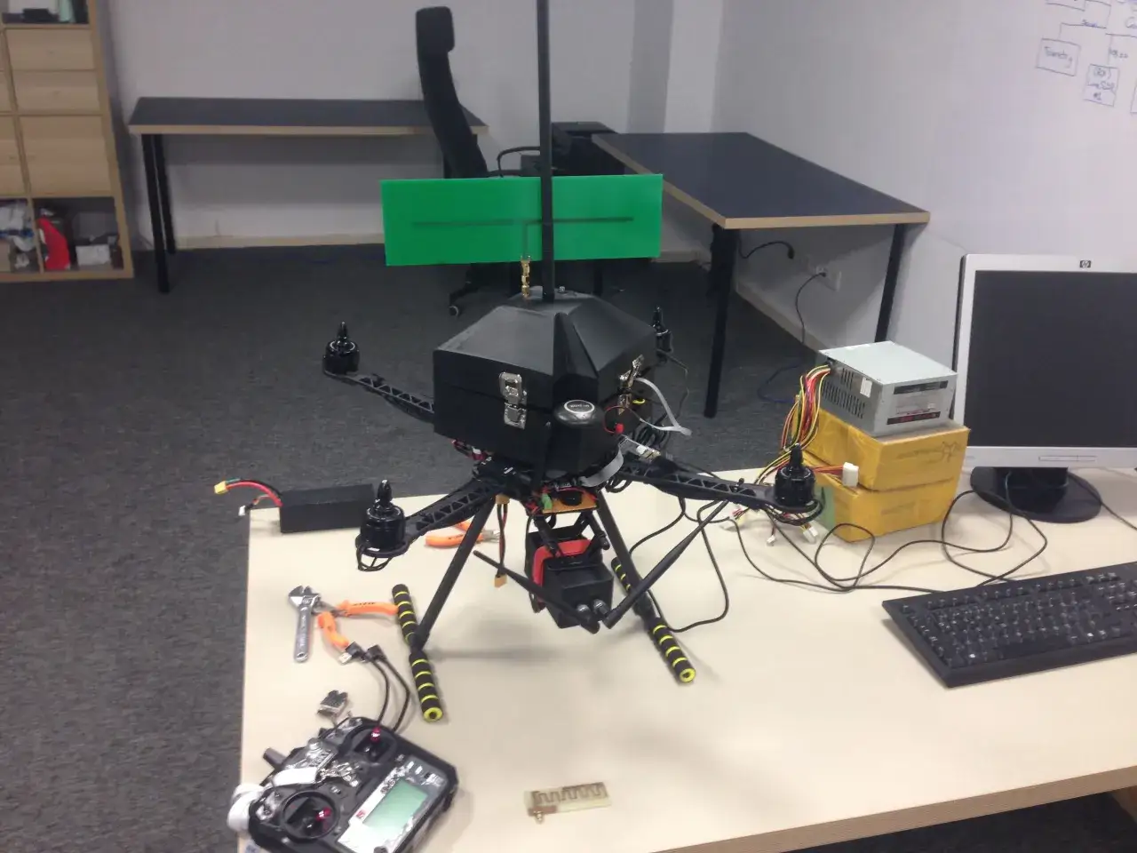 Dron z zieloną anteną, gotowy do testów zasięgu. Obok pilot, zasilacz i narzędzia.