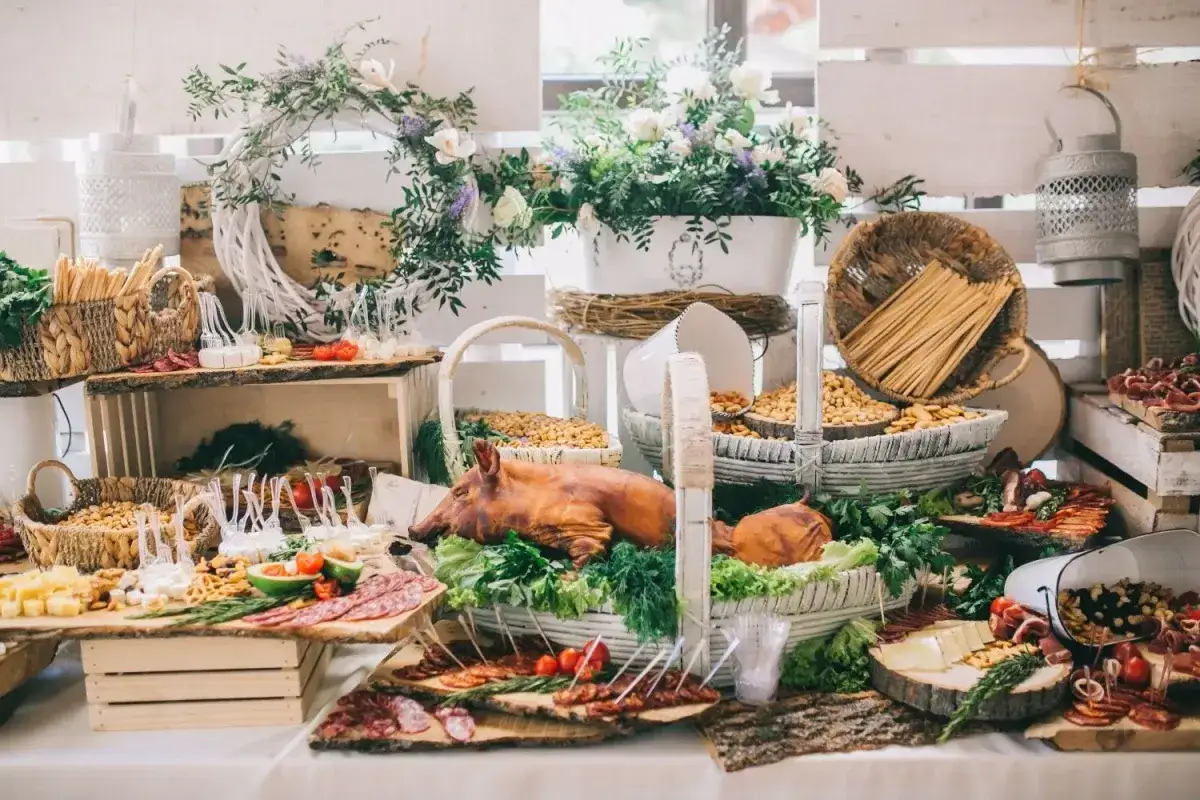 Bogaty stół z tradycyjnym menu weselnym: pieczony prosiak, sery, wędliny, orzechy i dekoracje z kwiatów.