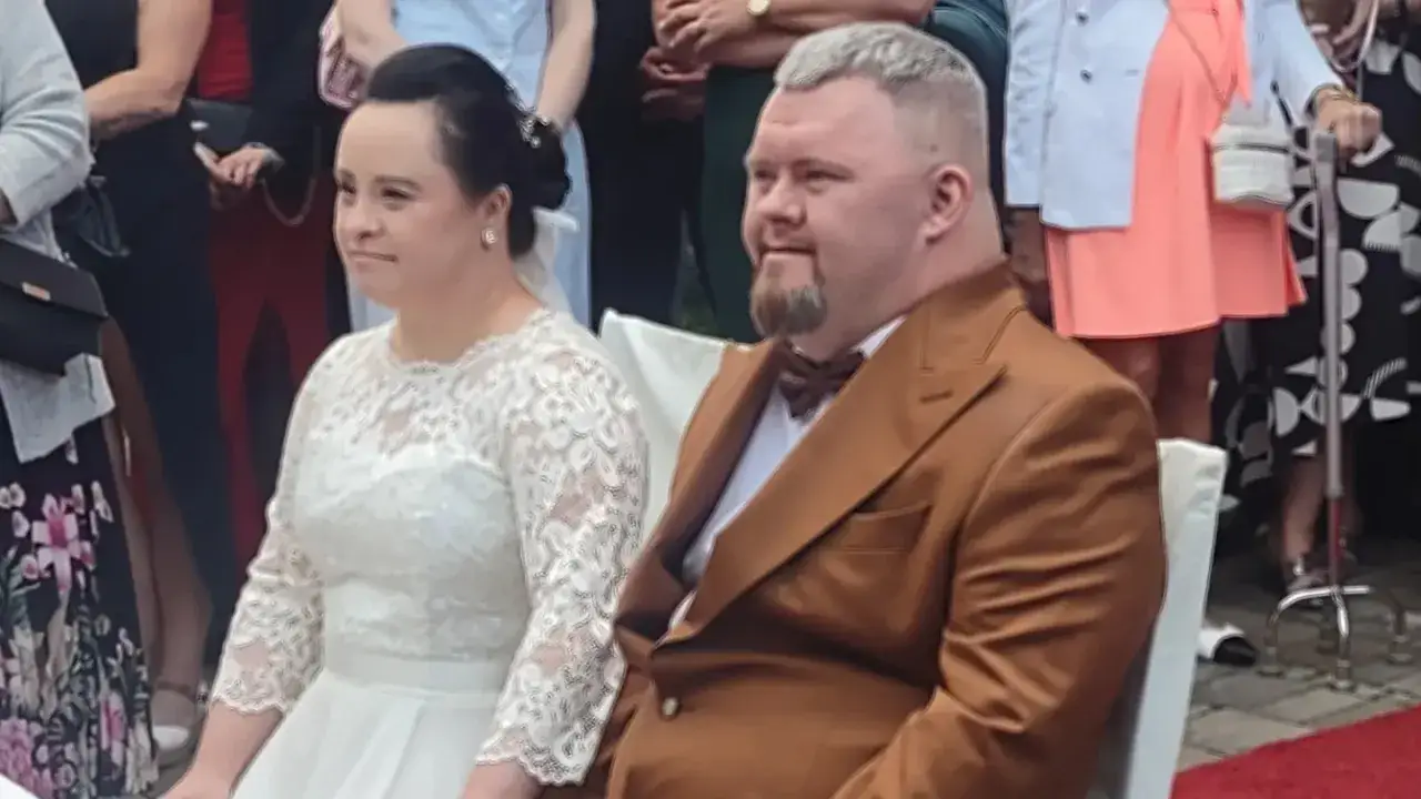 Para młoda w dniu ślubu. Ona w białej sukni, on w brązowym garniturze. Czy warto brać ślub? Ich uśmiechy sugerują, że tak!