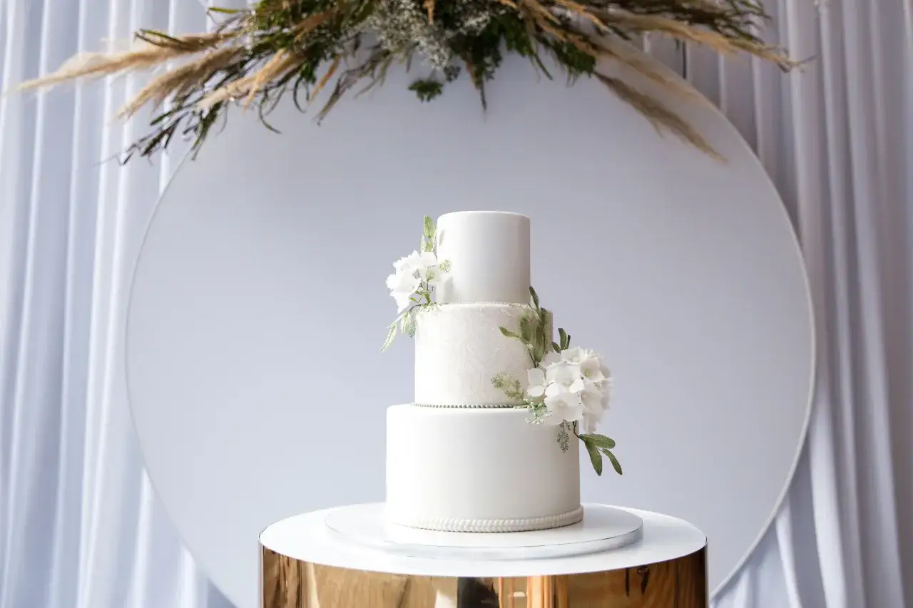 Elegancki, biały tort weselny z delikatnymi kwiatami i koronkowym wzorem. Piękne torty weselne, które zachwycają detalami.