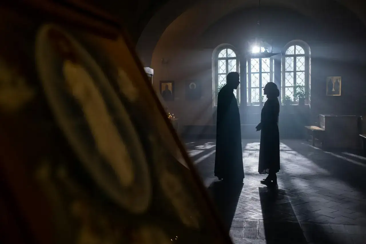Para młoda rozmawia z księdzem w kościele. Słońce wpada przez okna, tworząc magiczną atmosferę. To moment, kiedy płaci się księdzu za ślub.